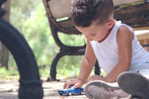 little boy in white shirt playing with a blue car at the park